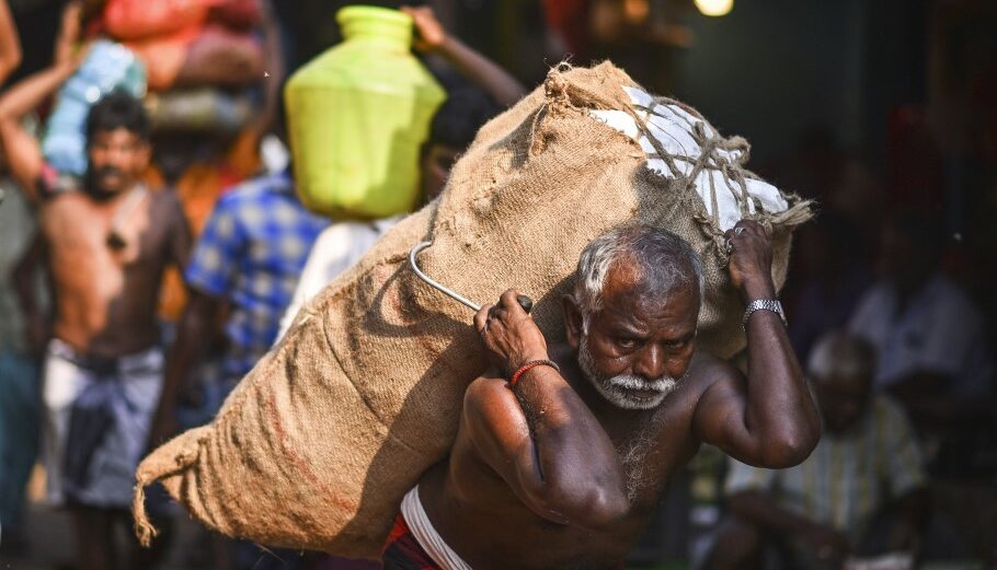 Εργάτης μεταφέρει σακί με λαχανικά σε υπαίθρια αγορά της Ινδίας © EPA/IDREES MOHAMMED